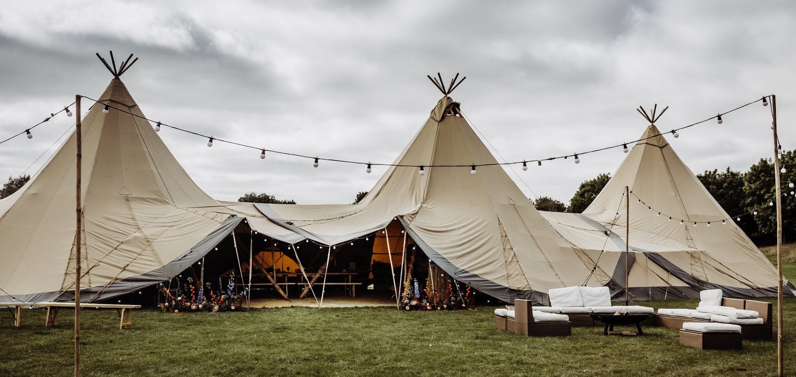 3 Giant Hat Tipis set up in a line with outdoor seating, fire pit and festoon lights on wooden poles