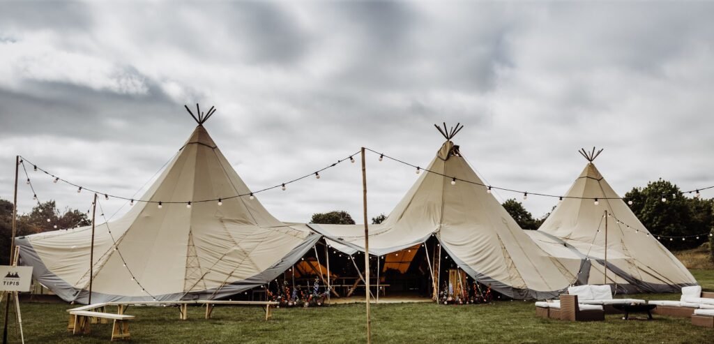 Three connected tipis with central entrance, outdoor seating area with fire pit to the right and ceremony area to the left.